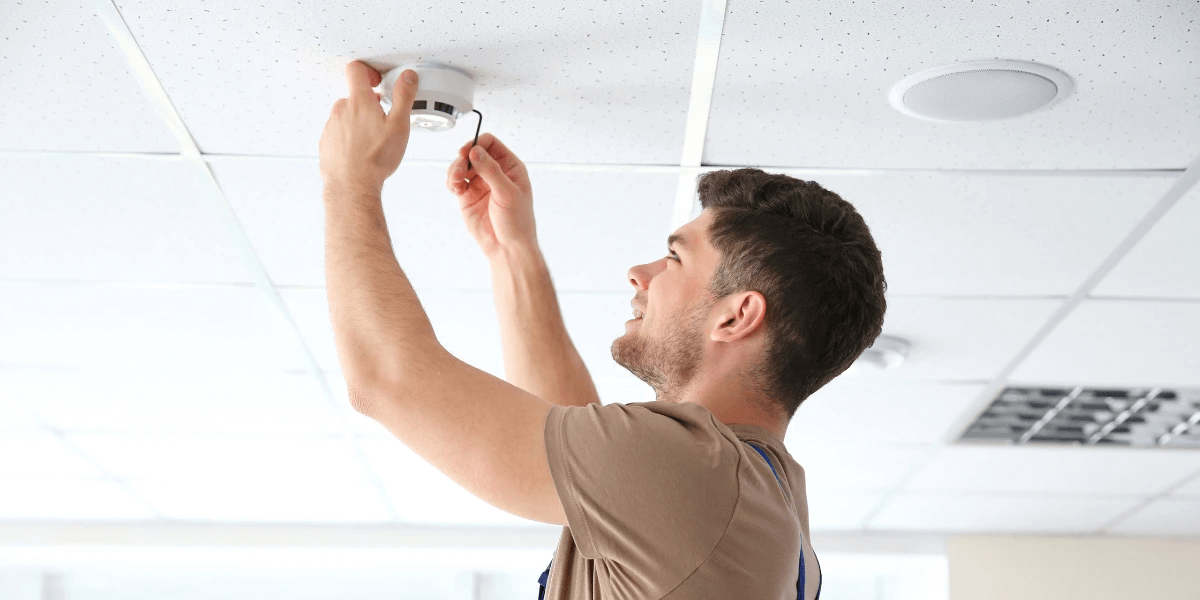 Electrician installing a smoke detector on the ceiling of an office